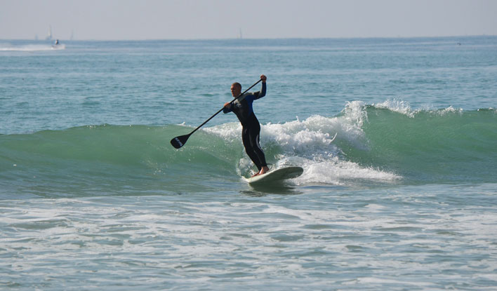 Ein SUP Paddler surft auf einer Welle